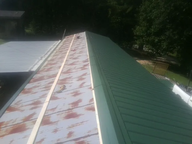 Old rusted panels beside newly installed green metal roofing — Wind Damage Roof Repair by Roofing Brothers in Neola
