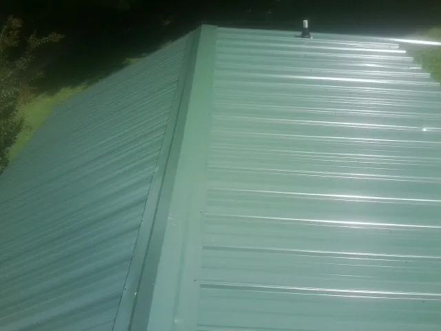 New green metal panels meeting at the ridge of a roof — Flat Roof Repair work by our crew in Neola
