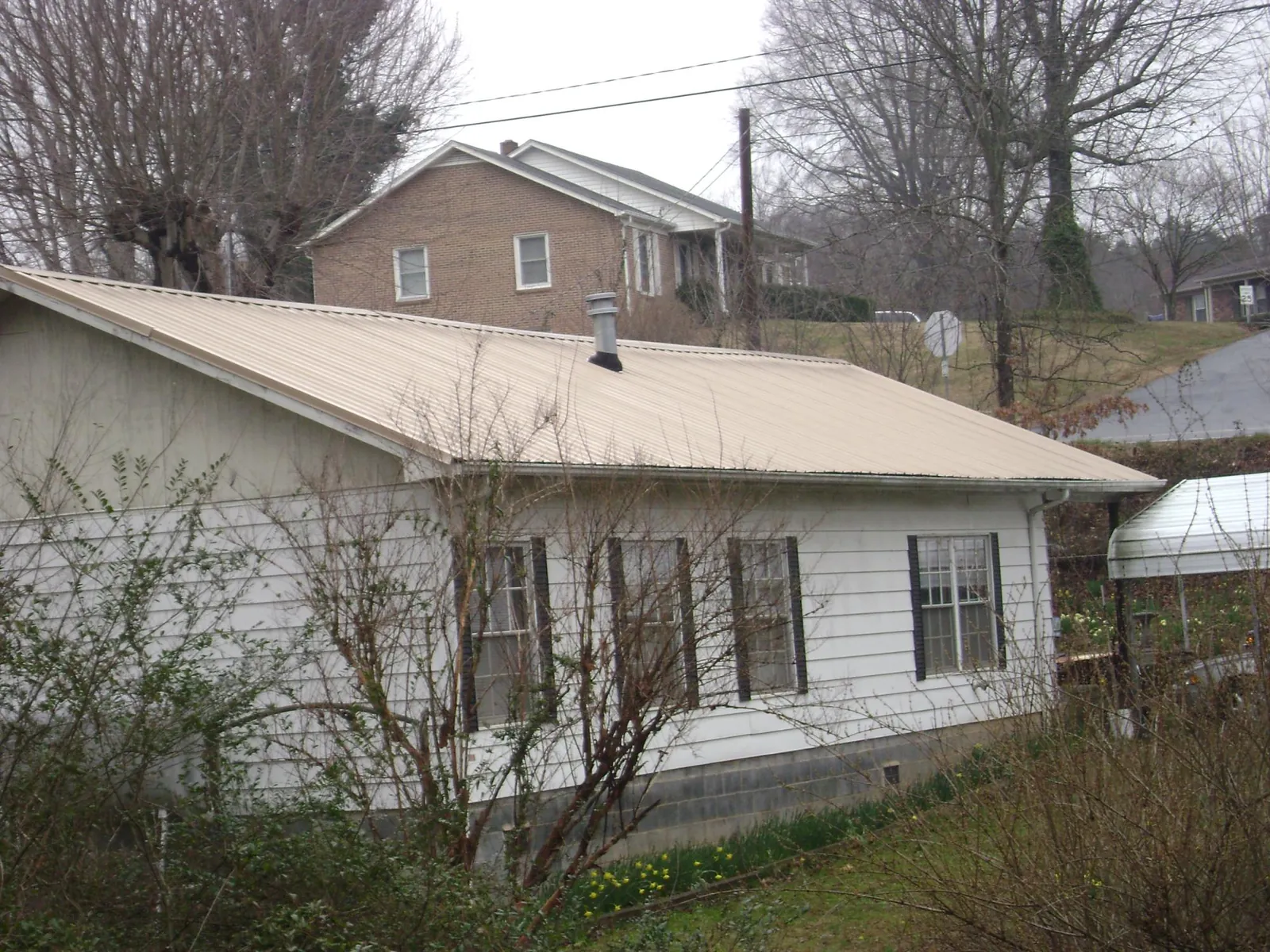 Tan metal roof on a white sided house set into a hillside — Commercial Roofing by Roofing Brothers in Neola