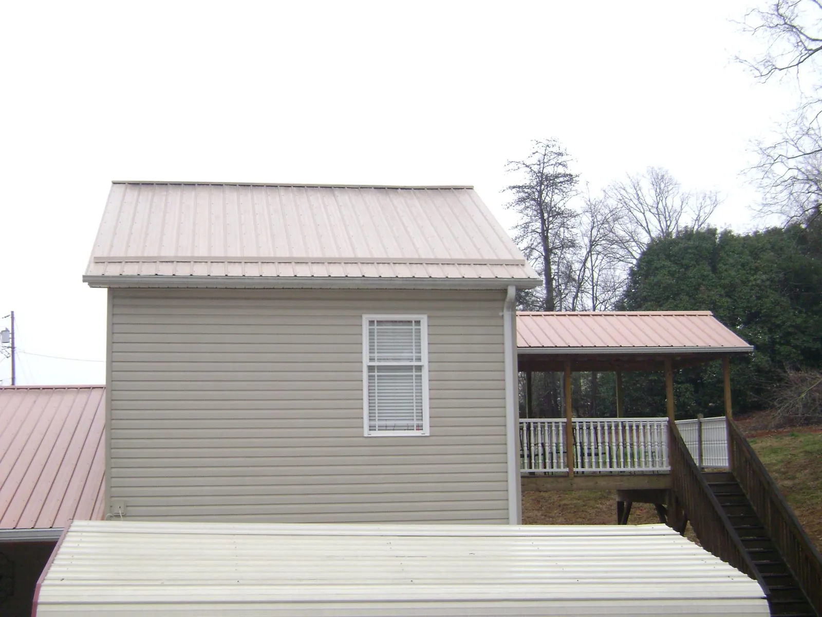 Tan metal roofs on a two story addition and attached porch, from a Roof Replacement job in Neola